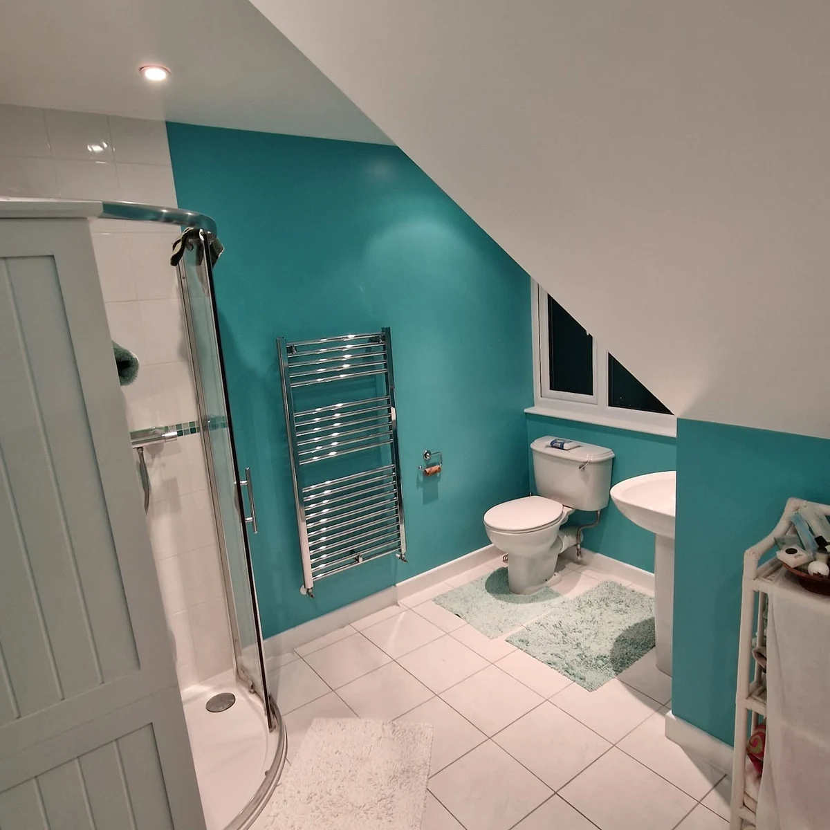 Loft bathroom with a teal feature wall, white sloped ceiling and corner shower