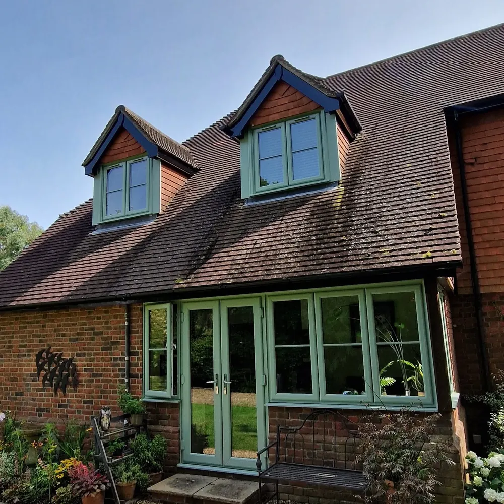 Brick cottage exterior with twin dormer windows and French doors painted in sage green