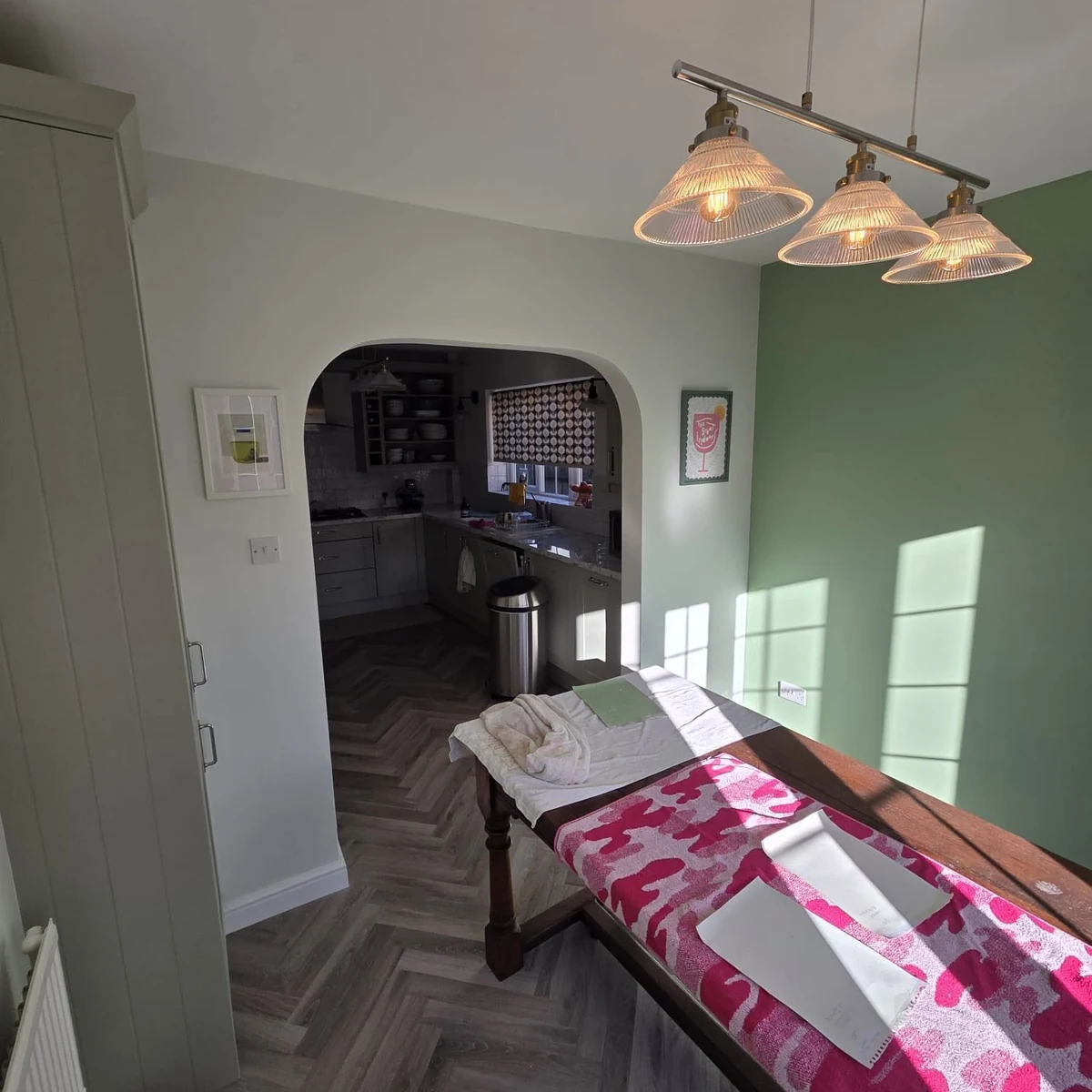 Dining room with sage-green painted walls and an archway through to the kitchen
