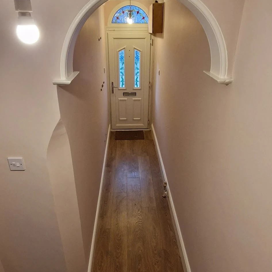Hallway with soft pink walls, white arch and coving leading to a stained-glass front door