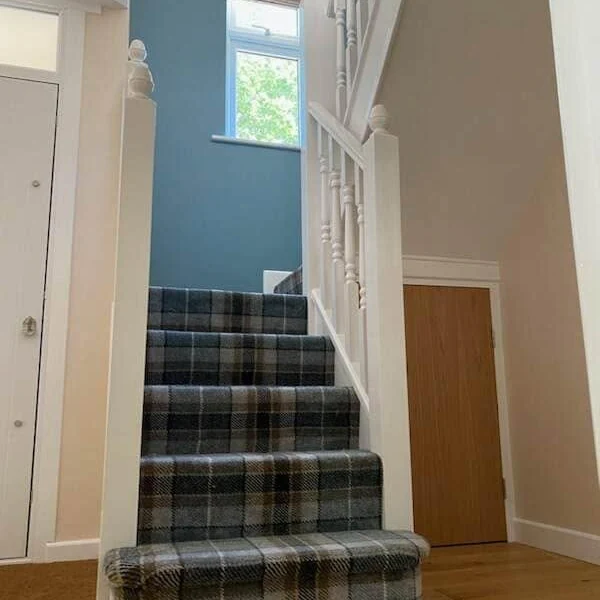 Staircase with a teal-blue feature wall, white spindles and a grey tartan stair runner